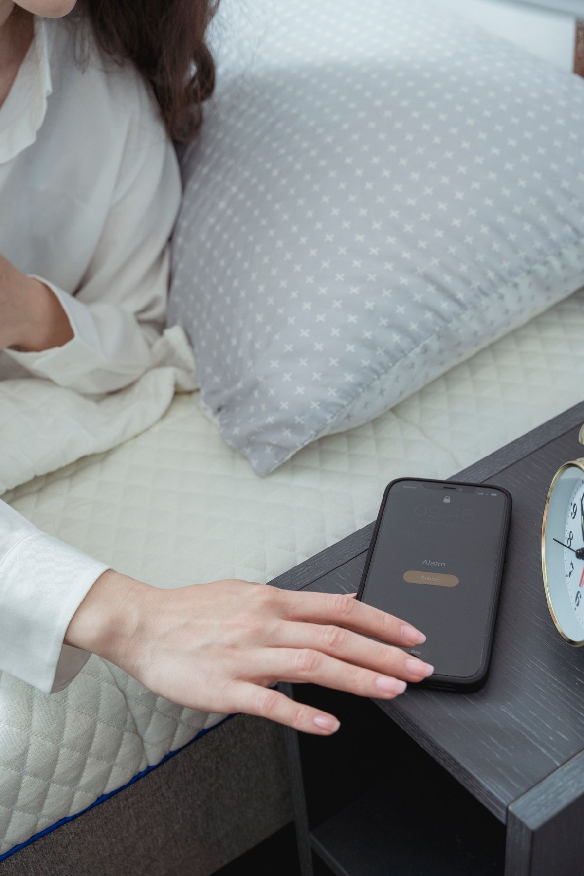 A person in bed reaching to snooze a smartphone alarm